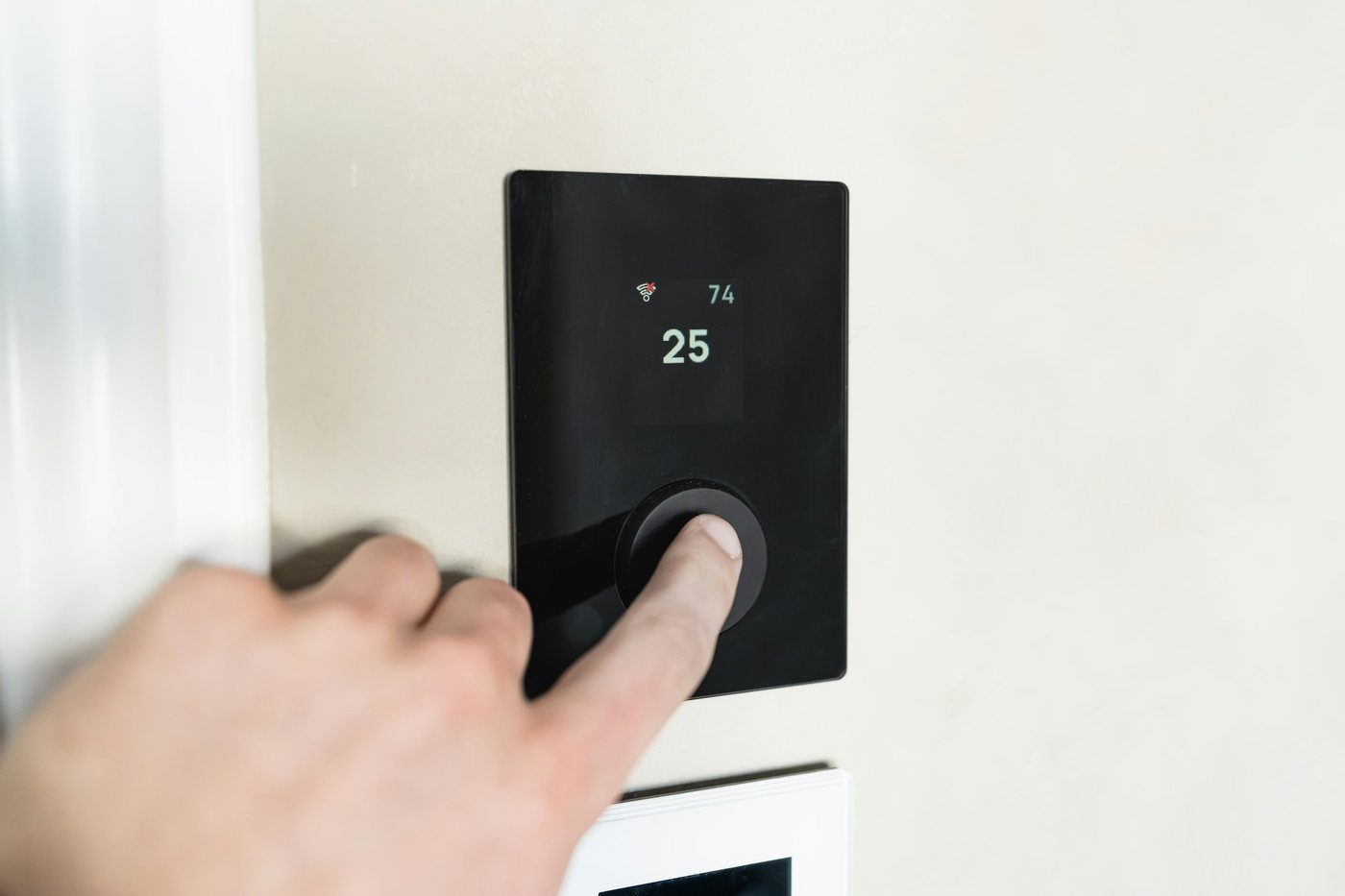 Dito che preme il pulsante di un termostato digitale a parete